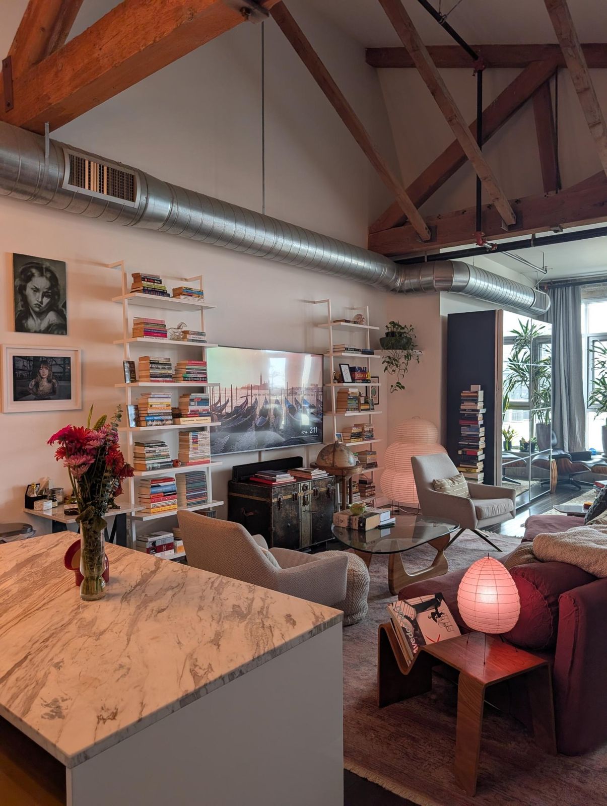 Living area seen from a marble kitchen island, with a glowing paper lamp and a low wood-and-glass coffee table.